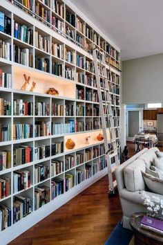 a living room filled with lots of books on top of a white book shelf next to a window