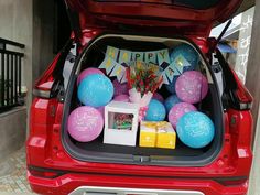 the trunk of a red car with balloons and presents in it