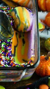 there are many halloween treats in the glass container with spoons and sprinkles