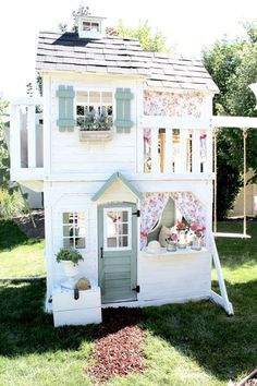 a white house with green shutters and flowers on the roof