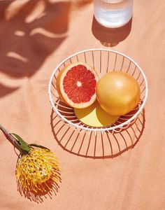 two grapefruits and an orange in a bowl on a table with a flower