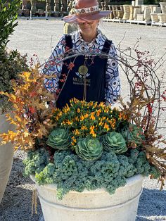 a woman in a cowboy hat standing next to a potted planter filled with succulents and flowers