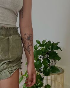 a woman with a flower tattoo on her left arm and right leg, next to a potted plant