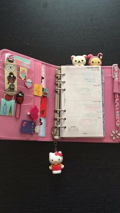 an open pink planner with hello kitty keychain hanging from it's side