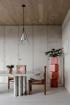 a dining room table with two chairs and a plant on the top of it in front of a white wall