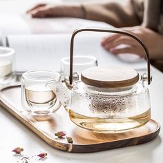 a glass tea pot and two cups on a tray