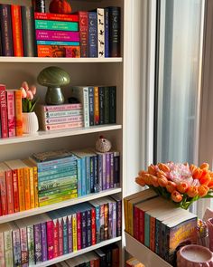 the bookshelves are full of colorful books and vases with flowers in them