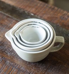 three white bowls stacked on top of each other in front of a wooden tabletop