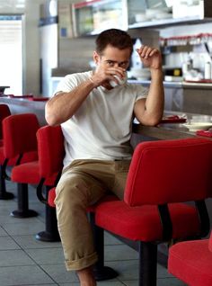 a man sitting at a table in a restaurant drinking from a cup with his hand on his mouth