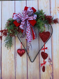 a heart shaped wreath with red and white bows hanging on a wooden wall next to two hearts