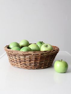 a wicker basket filled with green apples on top of a white counter next to an apple