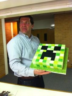 a man holding up a cake with green and black squares on it