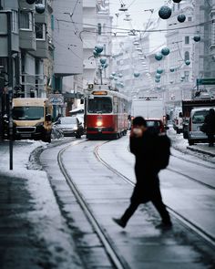 a man walking down a street next to a red bus on a city street covered in snow