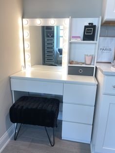 a white vanity with lights on it and a black stool in front of the mirror