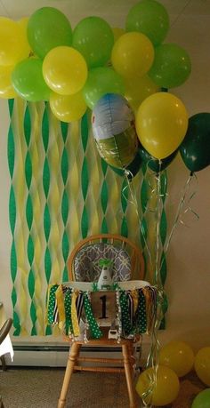 a baby's highchair with balloons and streamers on the wall behind it