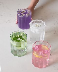 three different colored vases with flowers in them on a white countertop next to someone's hand