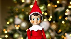 an elf doll sitting in front of a christmas tree