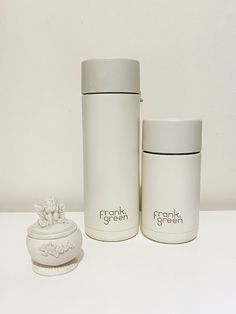 two white ceramic containers sitting next to each other on a table with a small figurine