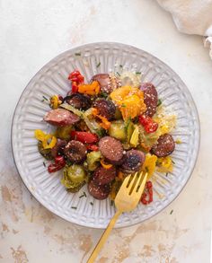 a white plate topped with sausage and vegetables next to a yellow fork on top of a table