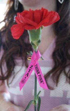 a woman holding a red flower with a pink ribbon on it