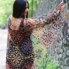 a woman standing next to a stone wall holding a shawl