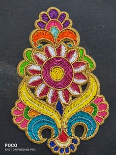 an embroidered patch with colorful flowers and leaves in the center, on a black surface