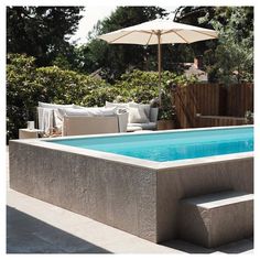 an empty swimming pool in the middle of a backyard with lounge chairs and umbrellas