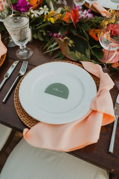 a place setting with plates, silverware and napkins on a wooden table surrounded by flowers