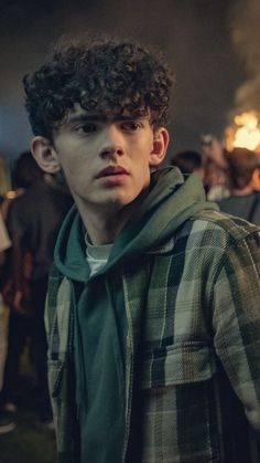 a young man with curly hair wearing a green hoodie standing in front of a crowd