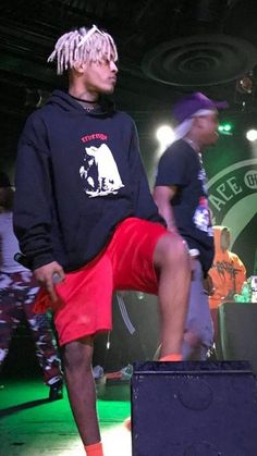 two young men sitting on top of a purple box at a concert, one with dreadlocks and the other without