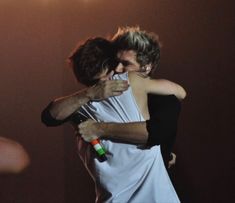 two people hugging each other on stage with lights in the backgroung behind them