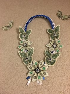 a necklace made out of dollar bills with butterflies flying around it and on the ground