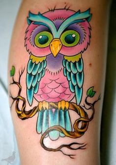 an owl tattoo on someones leg with green eyes and yellow beak, sitting on top of a branch