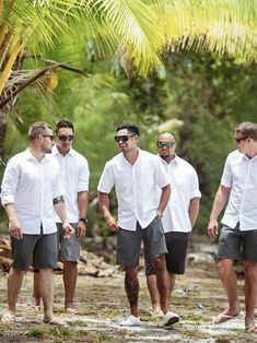 a group of men standing next to each other in front of a palm tree on the beach