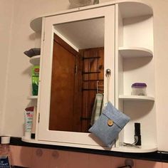 a bathroom sink with a medicine cabinet and mirror above it, in front of a wall mounted shelf