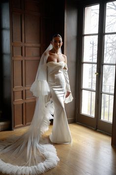 a woman in a white wedding dress standing on a wooden floor next to a window