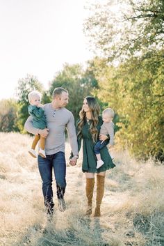 a man and woman holding their baby's hands while walking through tall grass