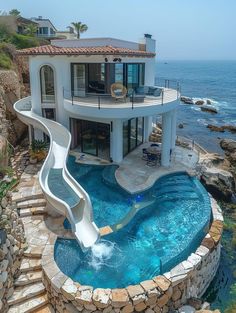 a house with a pool and slide in the middle of it by the water's edge