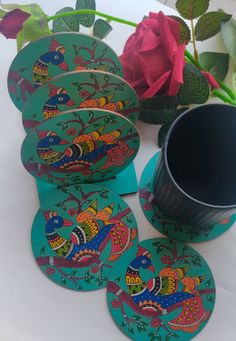 four coasters with colorful designs on them next to a vase and rose budding