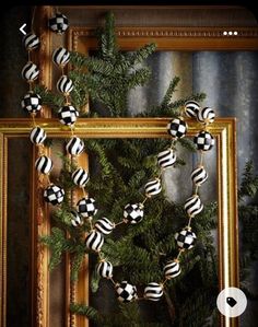 a christmas wreath with black and white ornaments hanging from it's sides in front of a gold frame