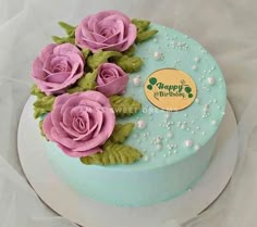 there is a blue cake with pink roses on the top and green leaves around it