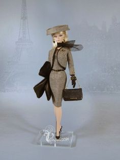 a barbie doll is holding a purse in front of the eiffel tower