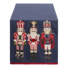 three wooden nutcrackers on a blue tablecloth with red pom - pom trim