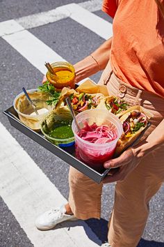 a person holding a tray full of food on the side of the road with drinks in it