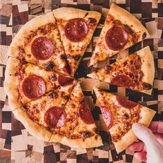 a person holding a slice of pepperoni pizza on top of a wooden cutting board