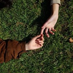 two people reaching out their hands to touch each other on the ground in the grass