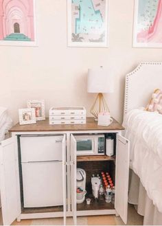 a small white refrigerator freezer sitting inside of a bedroom next to a bed and nightstand