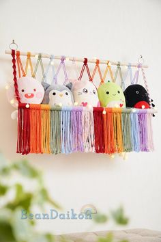 an assortment of stuffed animals hanging from a string on a white wall with green leaves