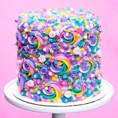 a multicolored decorated cake sitting on top of a white plate next to a pink wall