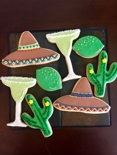 decorated cookies in the shape of cactuses and sombreros on a black tray